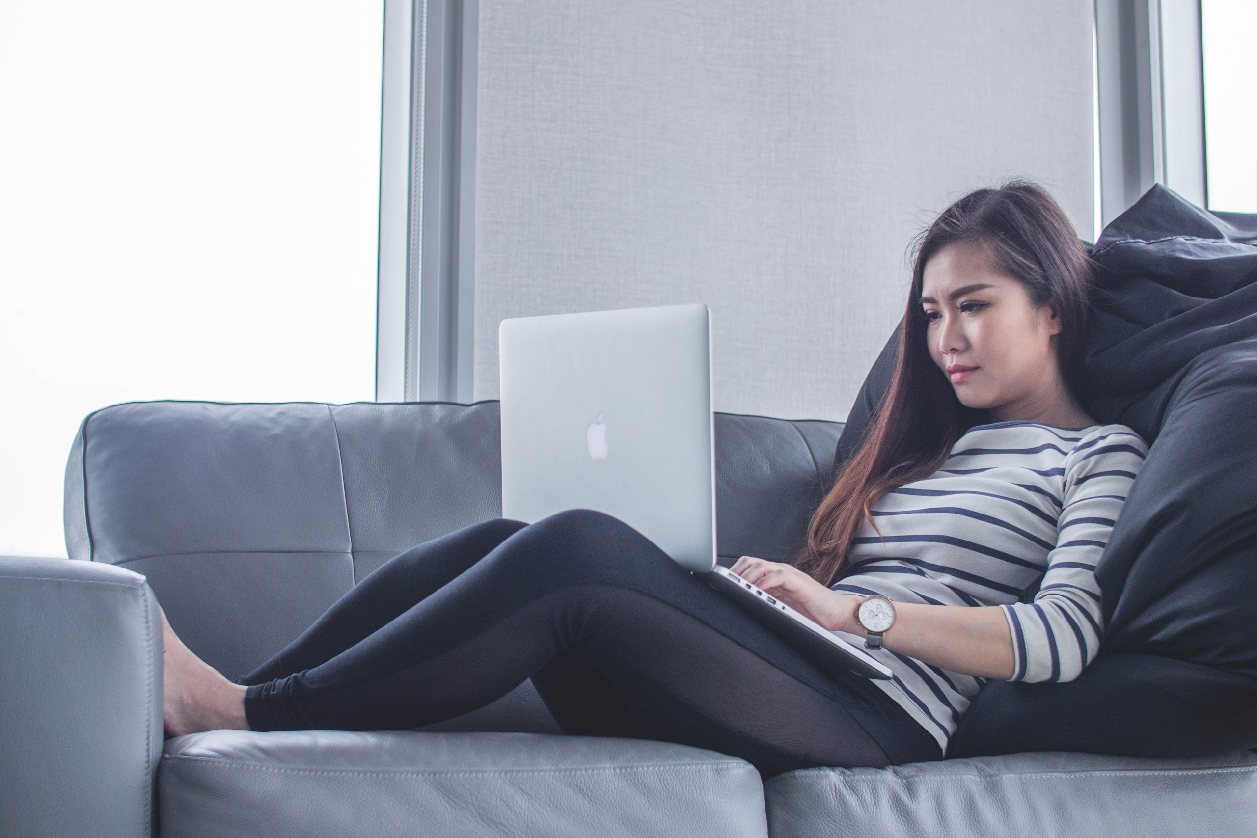 Woman lying on grey sofa browsing internet on a laptop